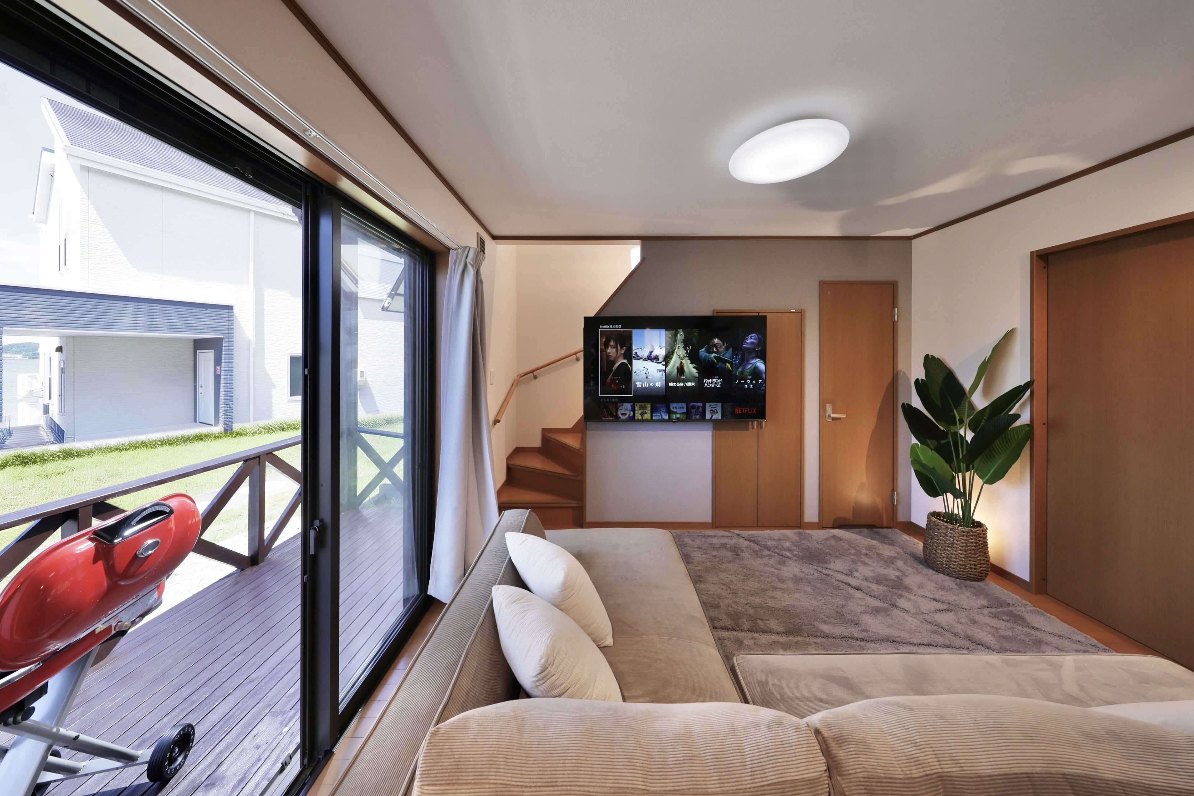 A modern interior with a large window, a flat-screen TV, a sofa, and a staircase.