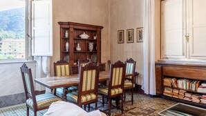A dining room with a wooden table and chairs, a cabinet with books, and a window with curtains. - Apartment 'Palazzo Ricci' with Wi-Fi (Carrara)
