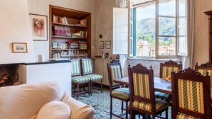 A room with a dining table, chairs, a bookshelf, a radiator, and a window with a view of buildings. - Apartment 'Palazzo Ricci' with Wi-Fi (Carrara)