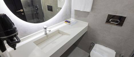 A modern bathroom with a white sink, a large mirror, a glass shower enclosure, and a toilet.