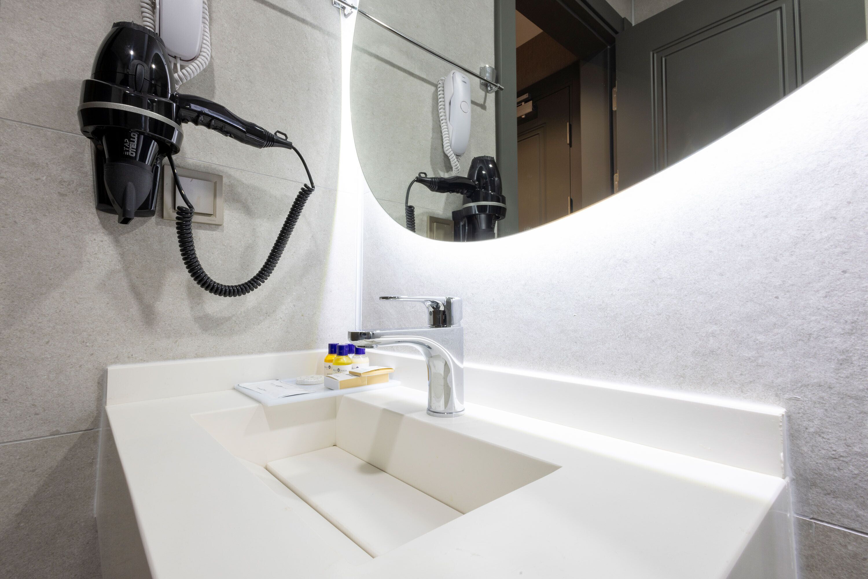 A modern bathroom with a white sink, a hairdryer, and a mirror.