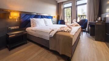 A hotel room with a large bed, a desk, a chair, and a balcony with a view.