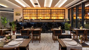 Un ristorante con pavimento in marmo, tavoli e sedie in legno. È presente un'area bar con bottiglie e una parete decorativa.