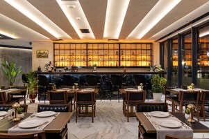A restaurant with a marble floor, wooden tables, and chairs. There is a bar area with bottles and a decorative wall.
