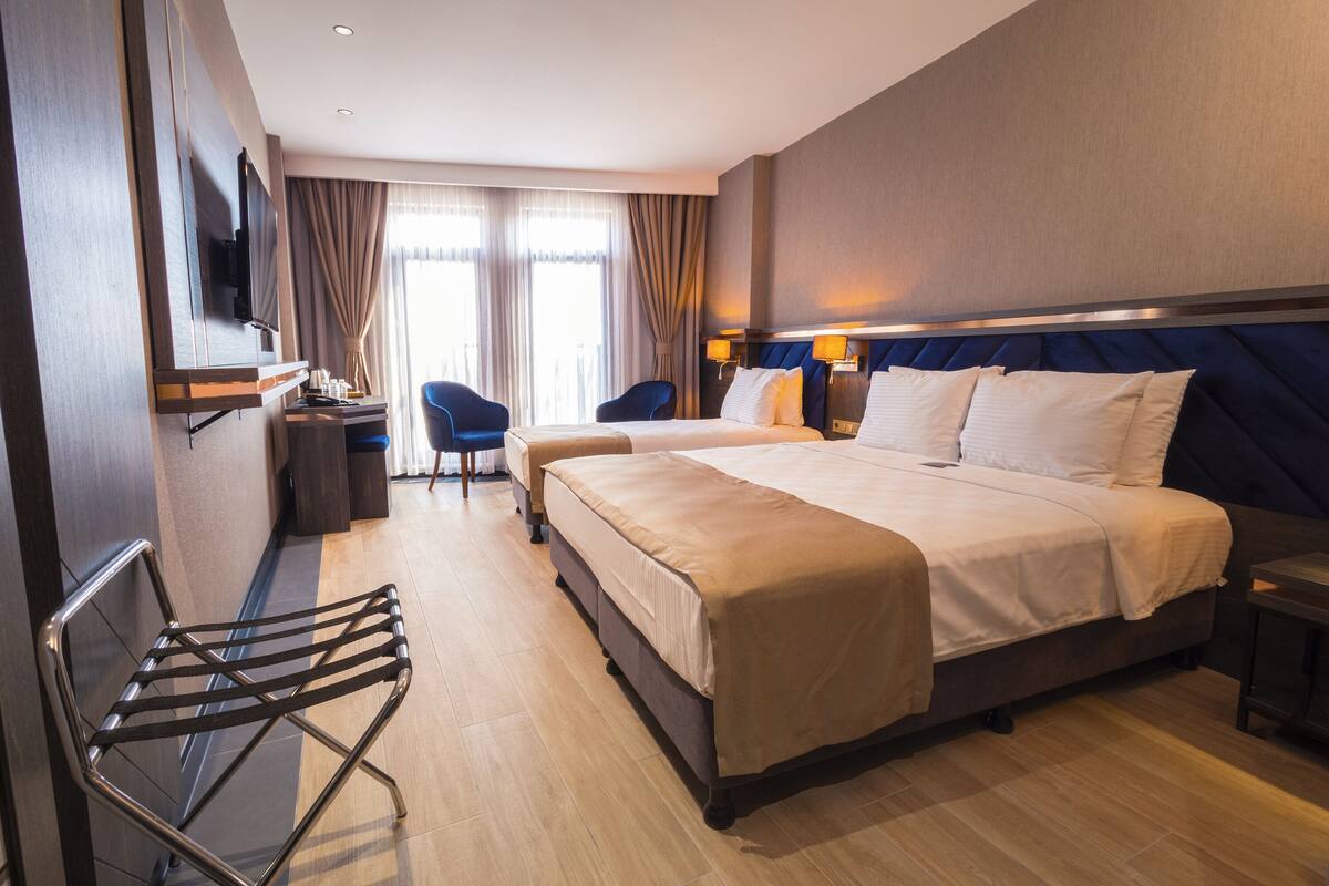 Een hotelkamer met een groot bed, een bureau met stoel, een aan de muur bevestigde televisie en een raam met gordijnen.