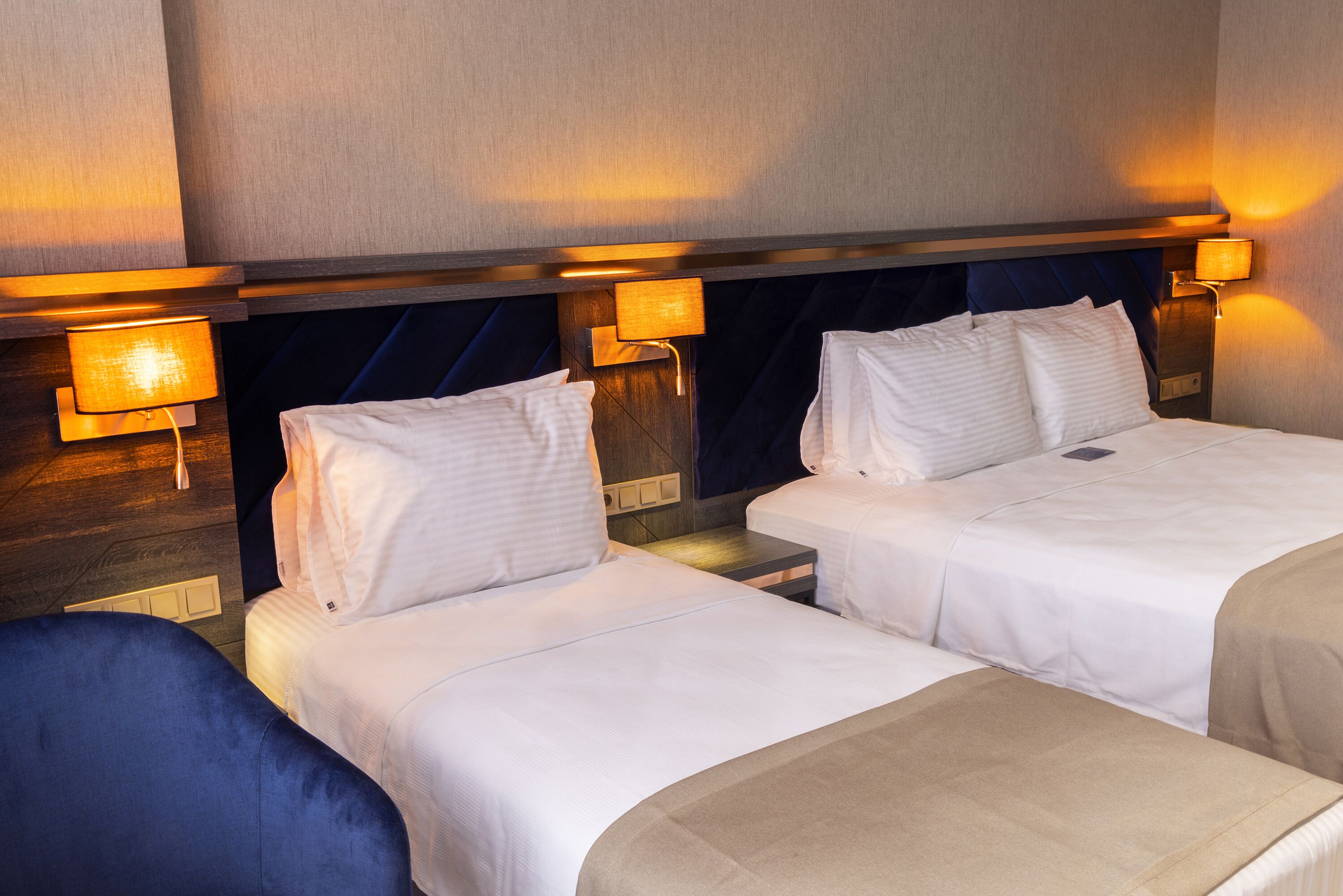 A hotel room with two beds, each with white linens and pillows, and bedside lamps.