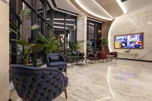 A modern lobby with a marble floor, leather sofas, and potted plants.