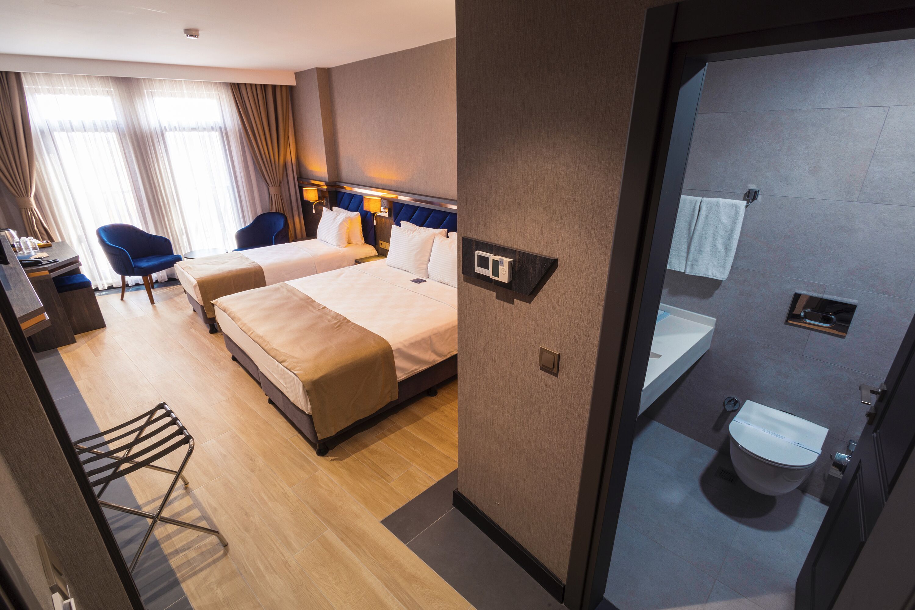 A hotel room with two beds, a desk, chairs, a bathroom, and a view of the city.