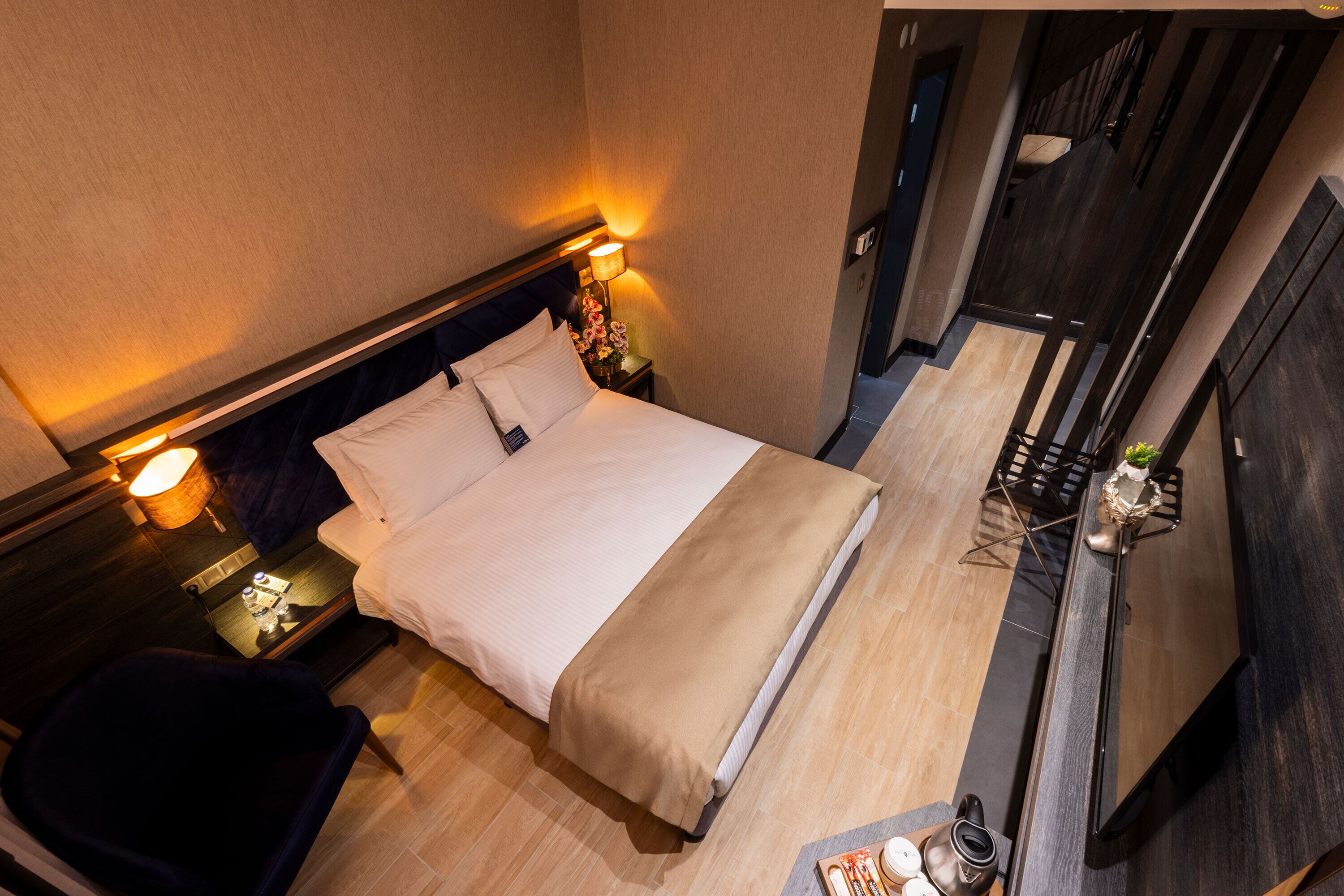 A hotel room with a bed, bedside tables, a chair, and a desk with a lamp.