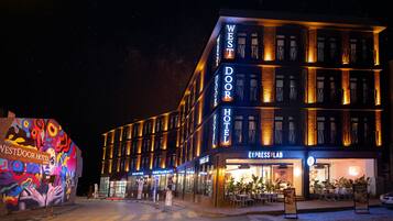 Un hotel de varios pisos con letreros iluminados que dicen "West Door Hotel" y "Express Lab" en la planta baja.
