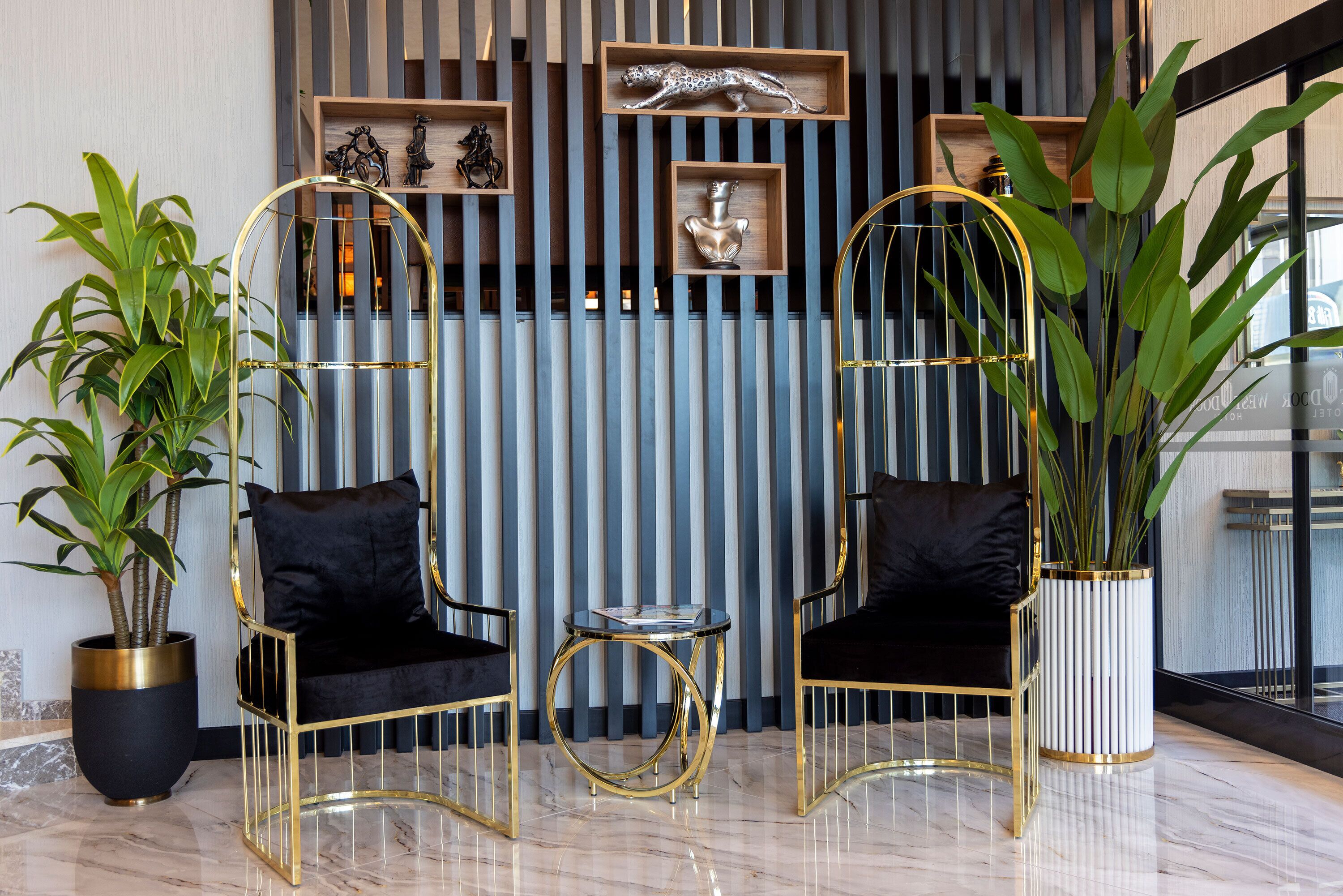 A modern interior with two gold-framed chairs, a small round table, and potted plants.