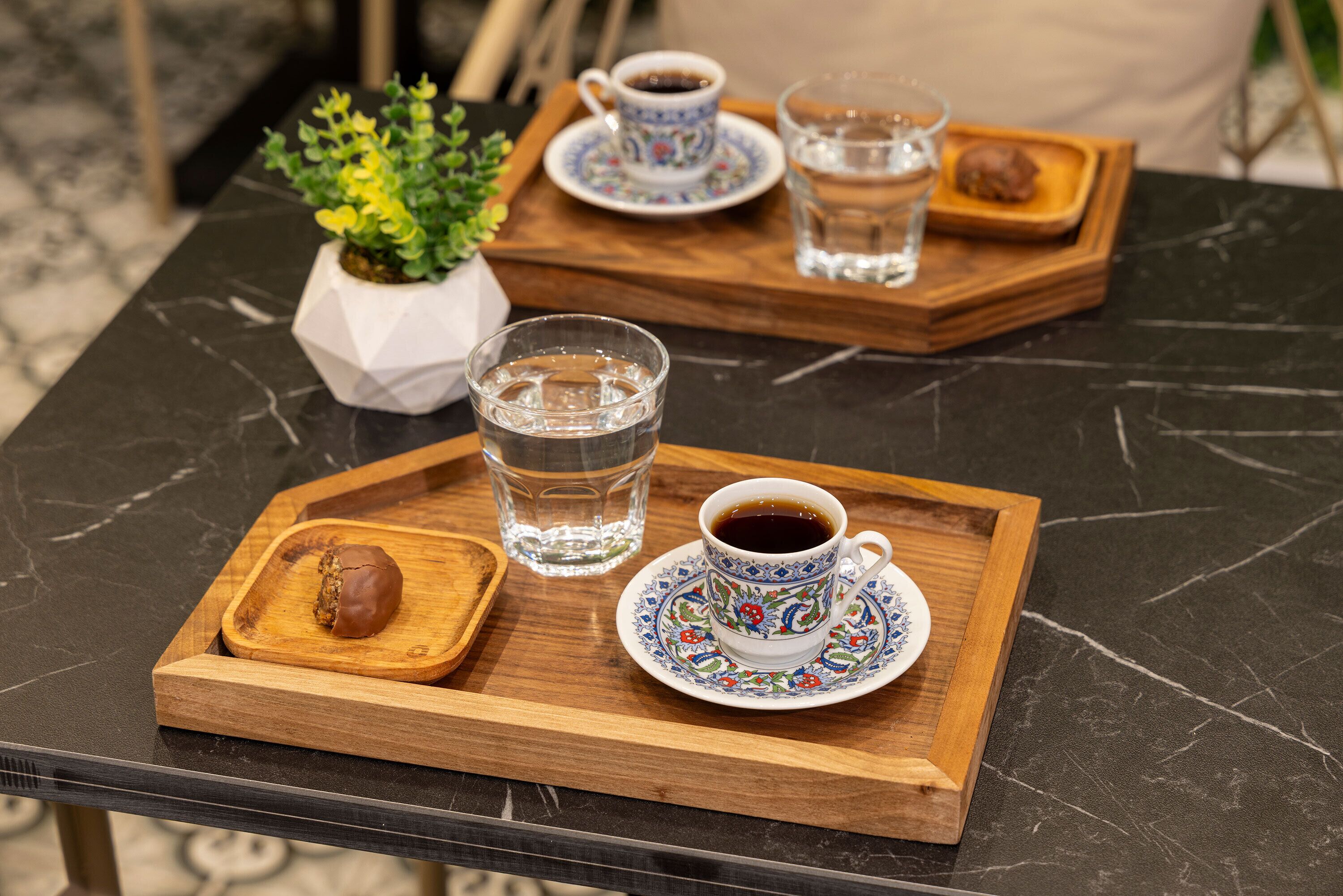 A tray with a cup of coffee, a glass of water, and a pastry on a marble table.