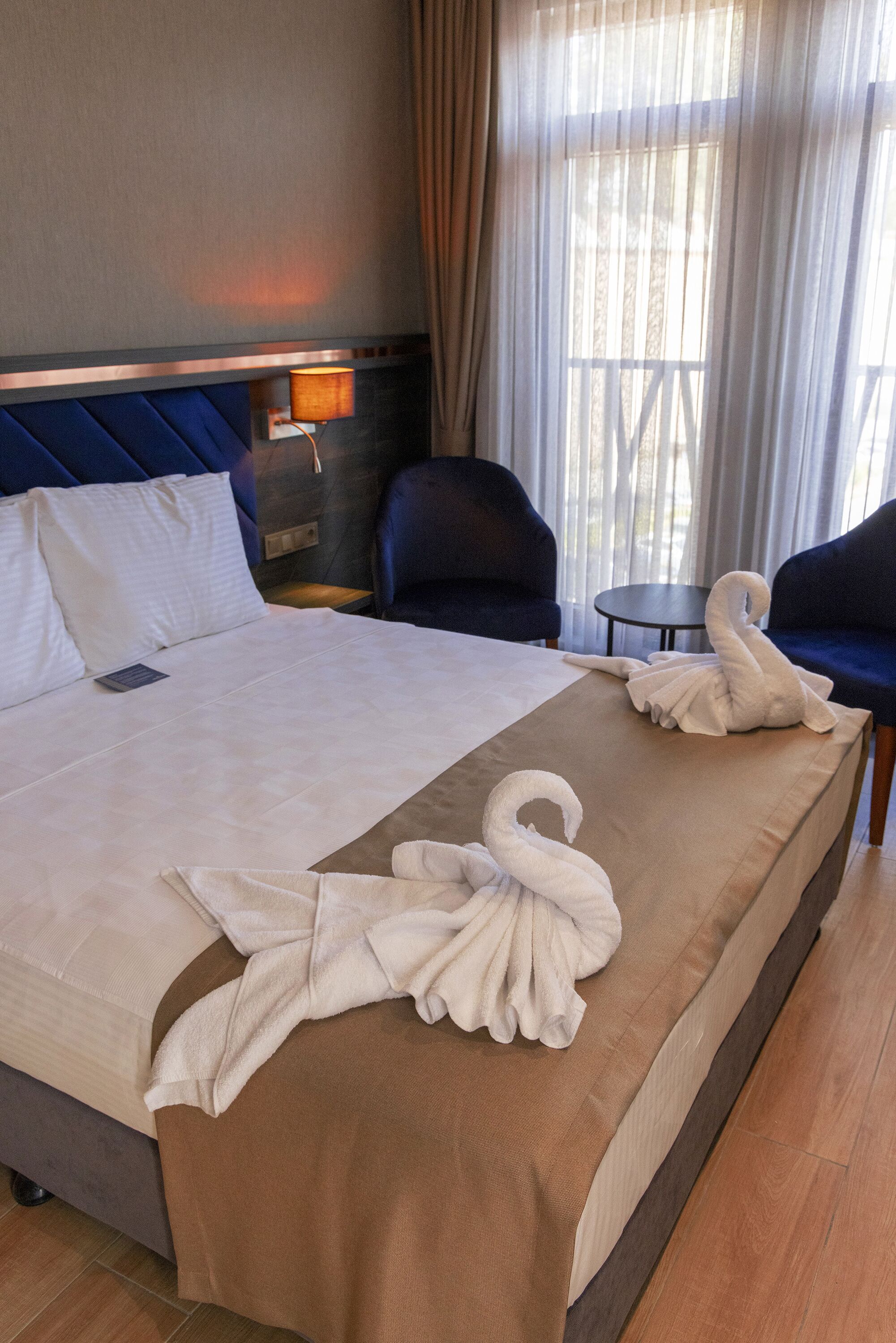 Une chambre d’hôtel avec un lit, deux chaises, une petite table et une fenêtre avec des rideaux.