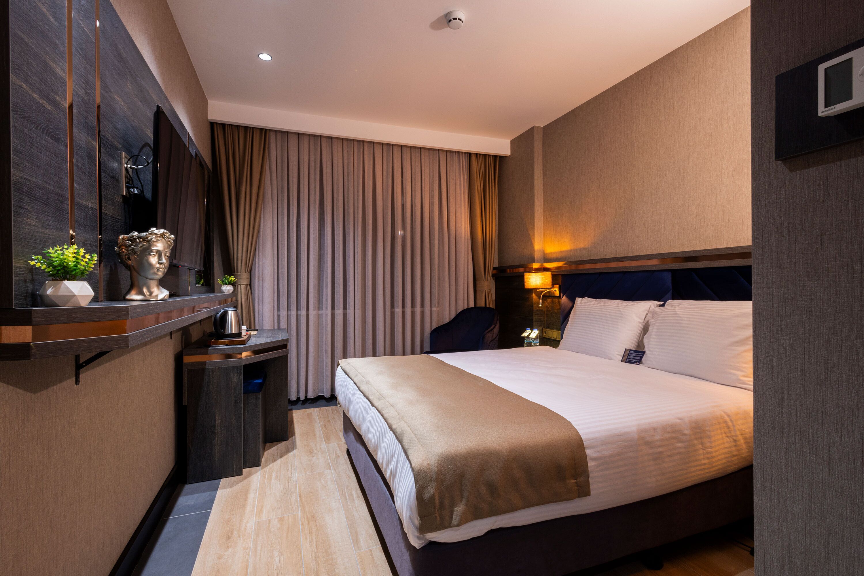 Habitación de hotel moderna con una cama grande, una mesita de noche, un espejo y vistas a la ciudad.