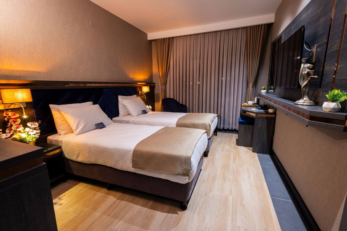 Een hotelkamer met twee bedden, een bureau, een stoel, een televisie en een groot raam met gordijnen.