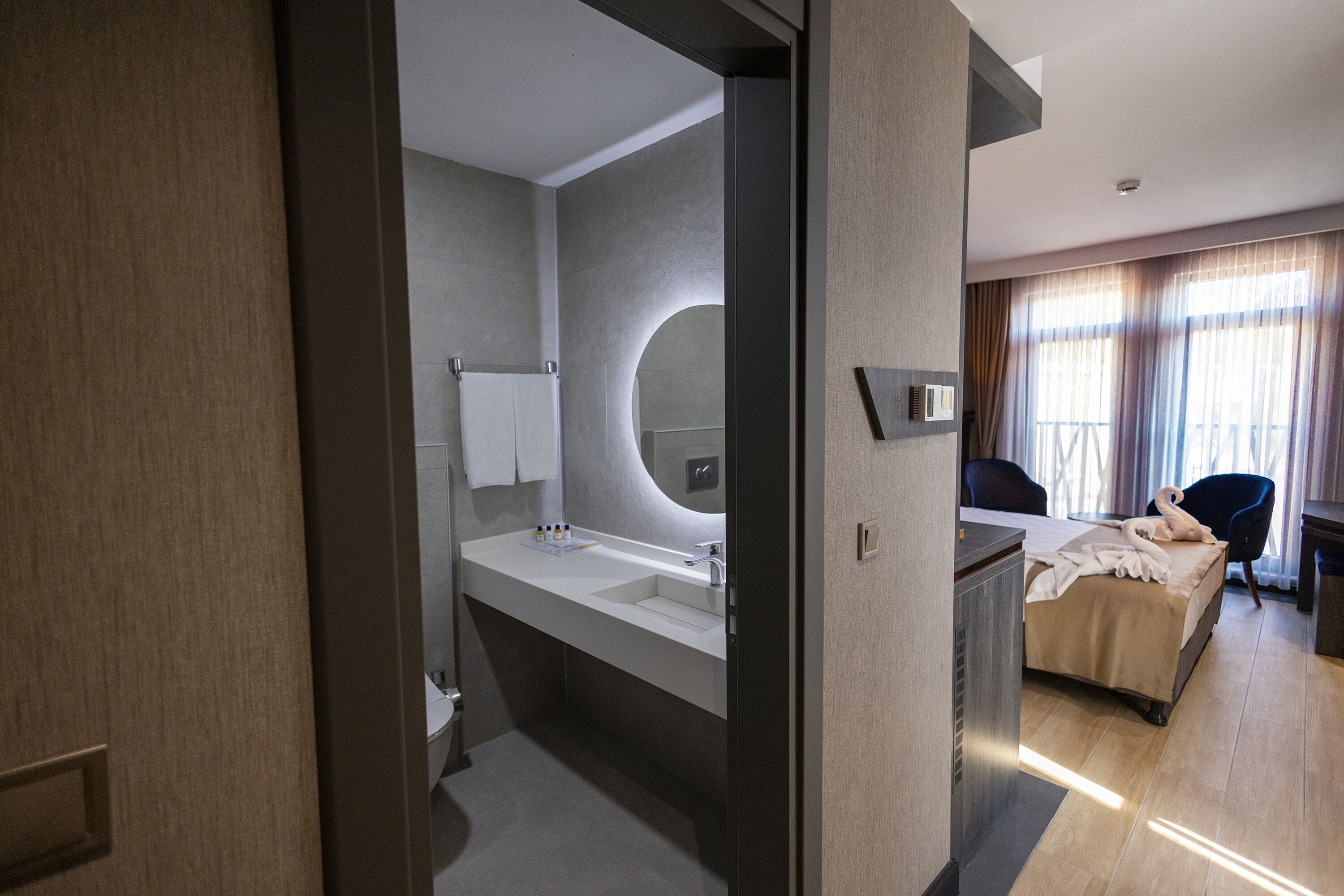 Une chambre d’hôtel moderne dotée d’un grand lit, d’une salle de bain séparée avec un lavabo et offrant une vue sur l’extérieur par la fenêtre.