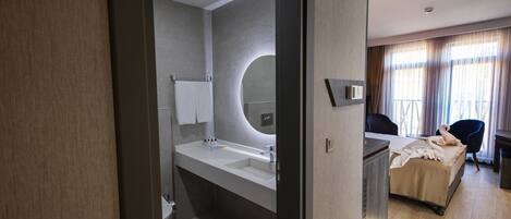 Une chambre d’hôtel moderne dotée d’un grand lit, d’une salle de bain séparée avec un lavabo et offrant une vue sur l’extérieur par la fenêtre.