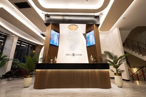 Un área de recepción de diseño moderno, con un mostrador de recepción, dos monitores y el logotipo del Hotel West Door.