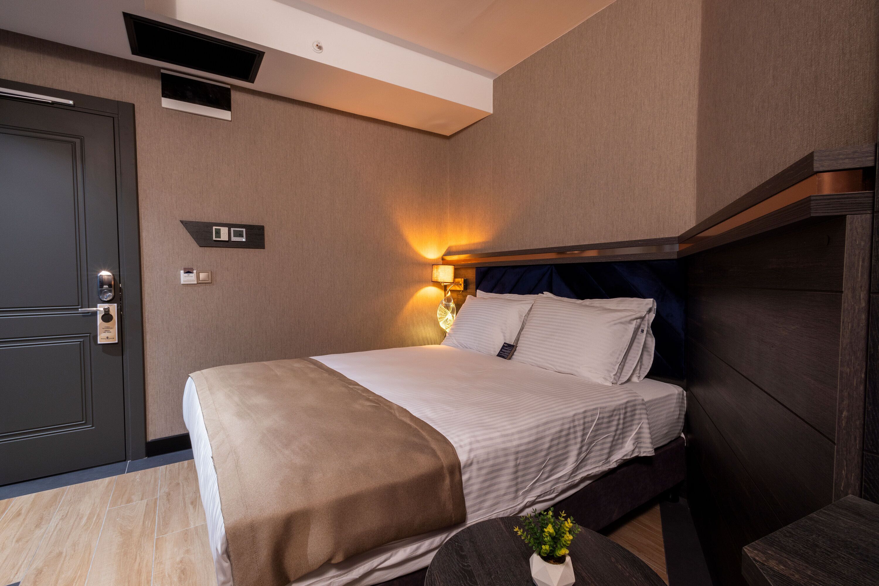 A hotel room with a bed, bedside table, and a wall-mounted light fixture.