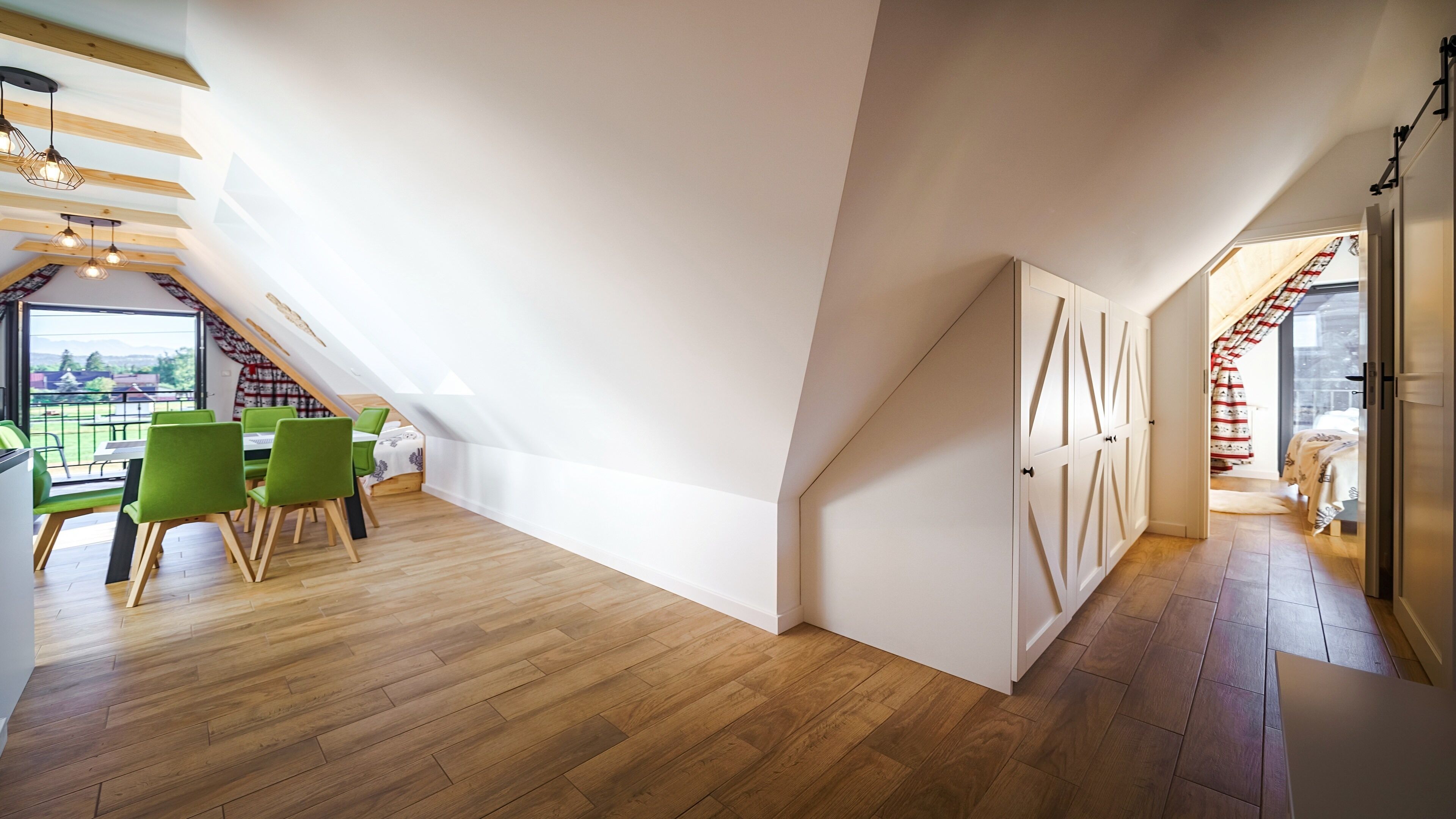 A spacious attic room with a dining area, wooden flooring, and a view of the outdoors.