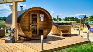 Uma sauna de madeira com porta, um banco e uma banheira de hidromassagem em uma estrutura circular de madeira.