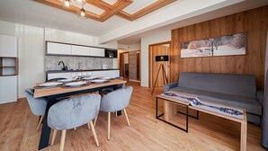 Uma sala de estar moderna com um sofá cinza, uma mesa de jantar posta com pratos e copos, e piso de madeira.