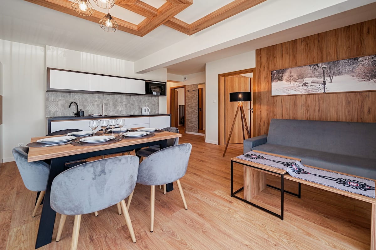 Ein modernes Wohnzimmer mit einem grauen Sofa, einem Esstisch mit Tellern und Gläsern sowie einem Holzboden.
