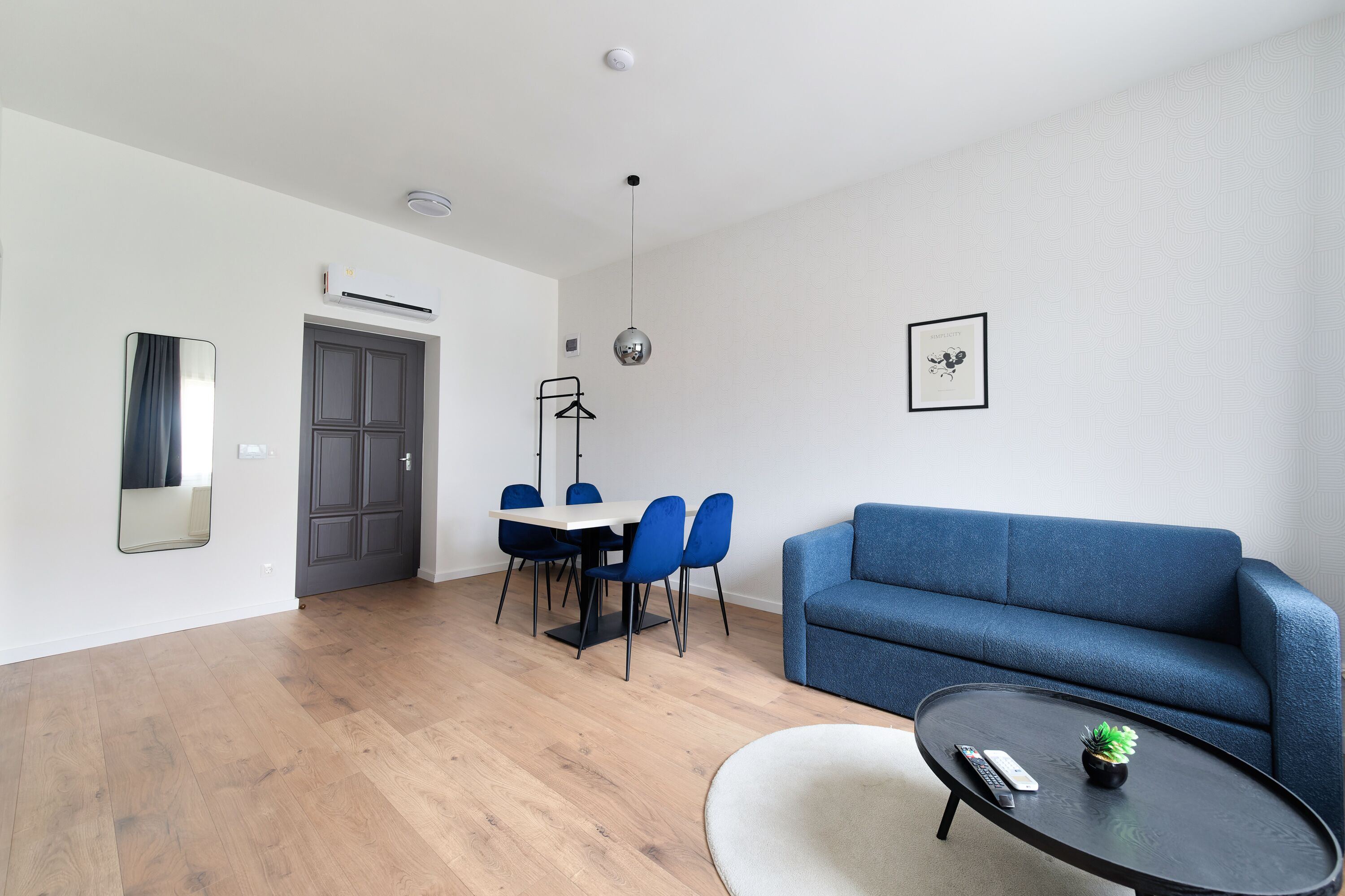 A modern living room with a blue sofa, a round coffee table, and a dining area with blue chairs and a white table.