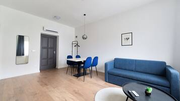 A modern living room with a blue sofa, a round coffee table, and a dining area with blue chairs and a white table.