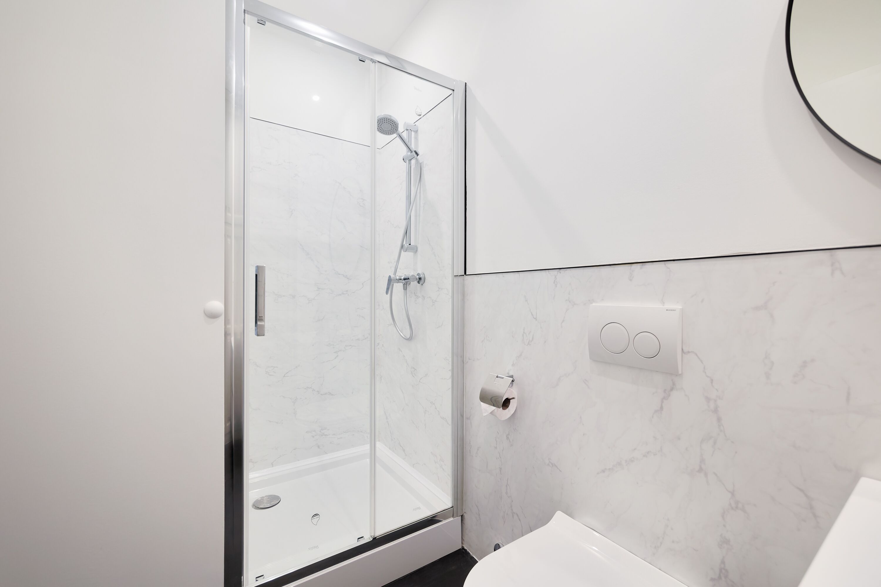 A modern bathroom with a glass-enclosed shower, a white sink, and a marble wall.