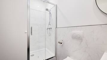 A modern bathroom with a glass-enclosed shower, a white sink, and a marble wall.