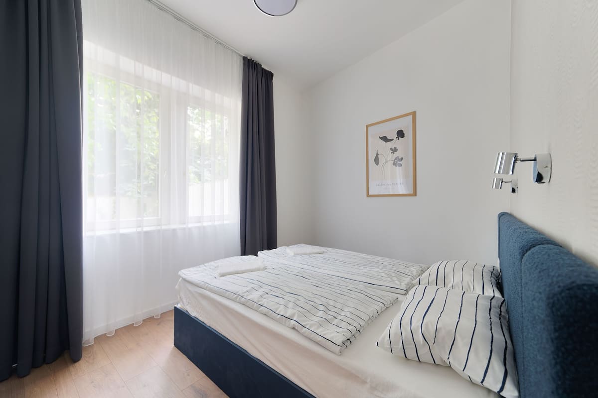 A bedroom with a bed, curtains, a framed picture, and a wall-mounted light fixture.