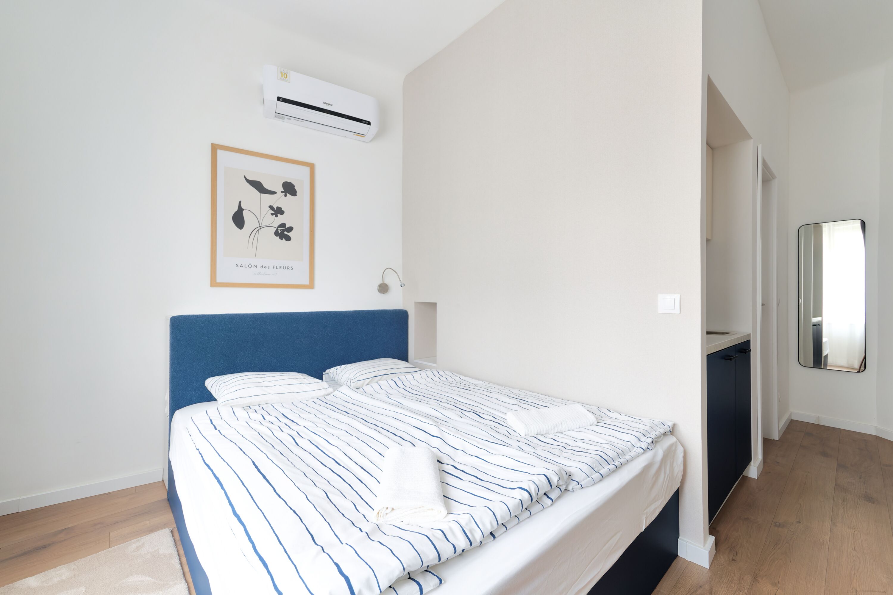 A neatly made bed with striped bedding, a blue headboard, and a framed botanical print on the wall.