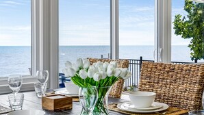 A dining area with a view of the sea, a chandelier, and wicker furniture. - 4 Bedroom Water's Edge Oasis with Salt Water Pool (Kingsville)