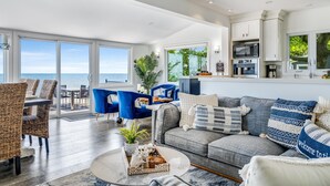 A spacious living room with a large window overlooking the ocean, a kitchen with modern appliances, and comfortable seating areas. - 4 Bedroom Water's Edge Oasis with Salt Water Pool (Kingsville)
