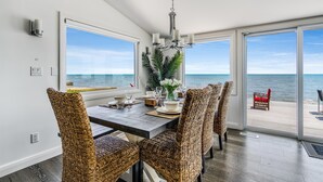 A dining area with a view of the ocean, wicker chairs, a chandelier, and a table set for four. - 4 Bedroom Water's Edge Oasis with Salt Water Pool (Kingsville)