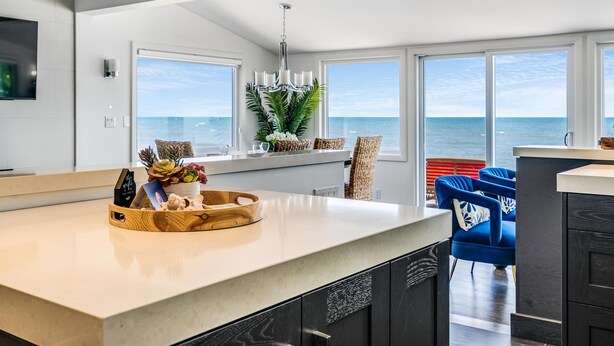 A modern kitchen with a large island, white cabinetry, and a view of the ocean. - 4 Bedroom Water's Edge Oasis with Salt Water Pool (Kingsville)