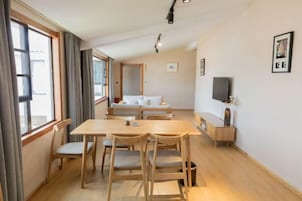 Um quarto com uma mesa de jantar, cadeiras, um sofá, uma televisão e uma janela com cortinas.