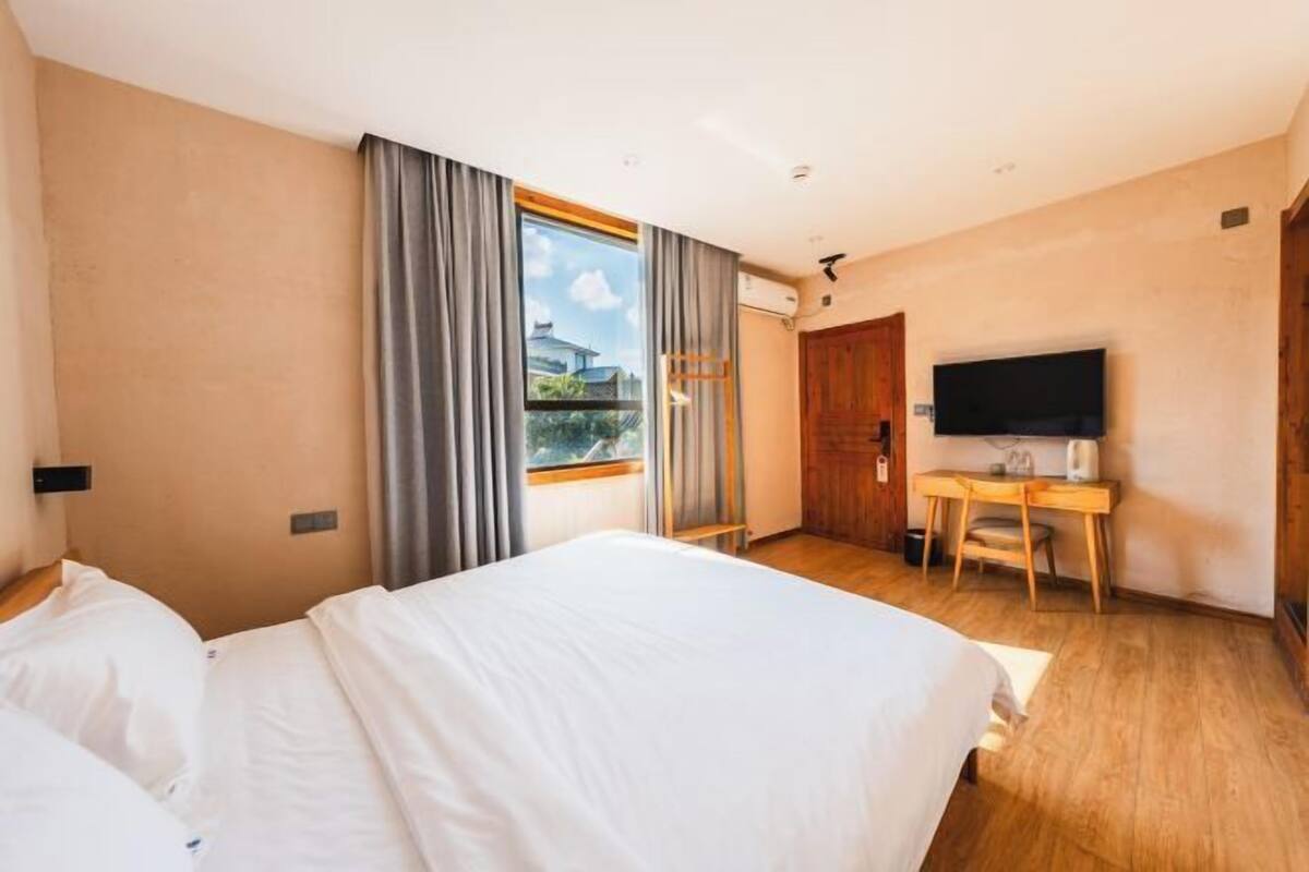A hotel room with a bed, a desk, a TV, and a window with curtains.