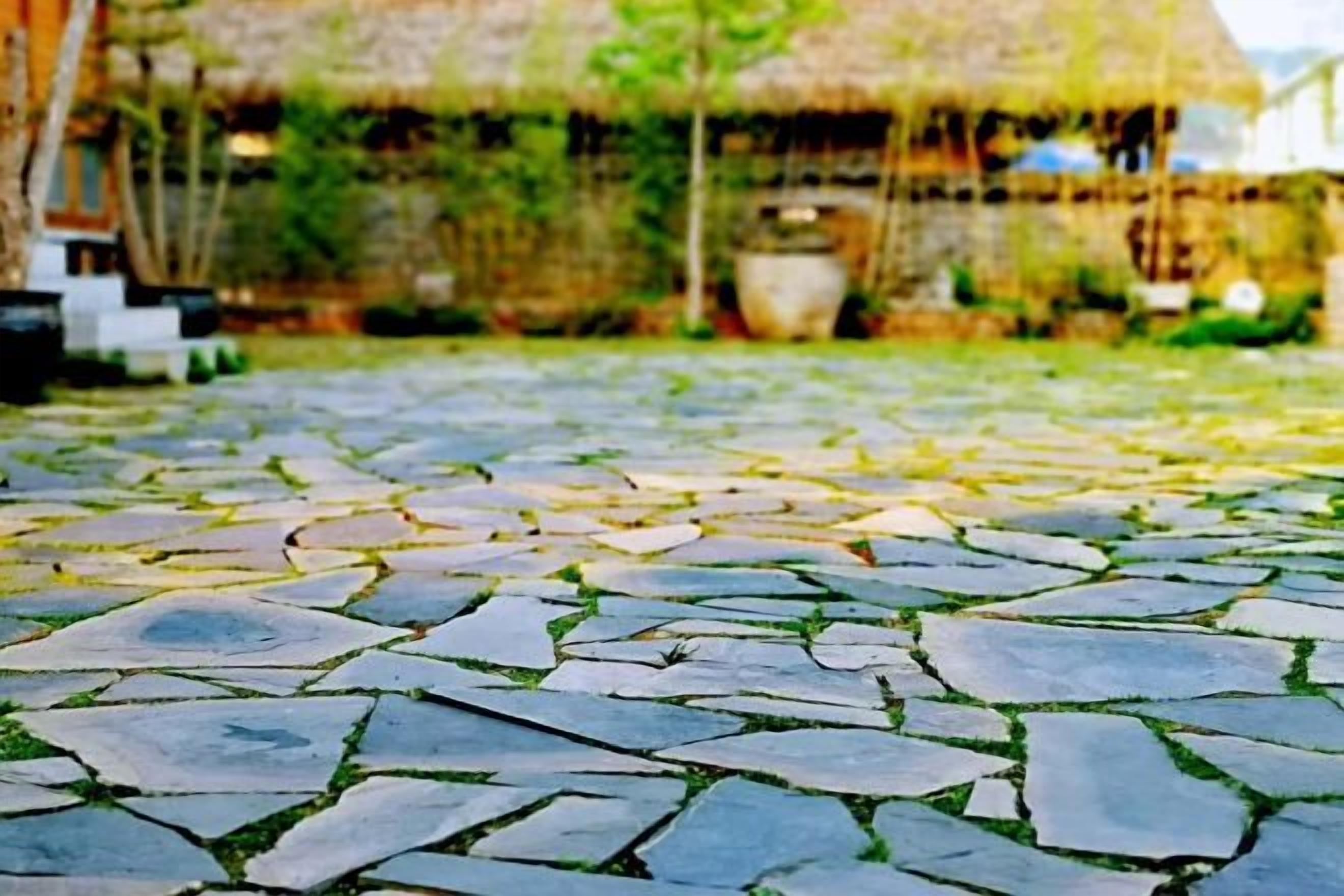 A stone-paved courtyard with a thatched-roof structure in the background.