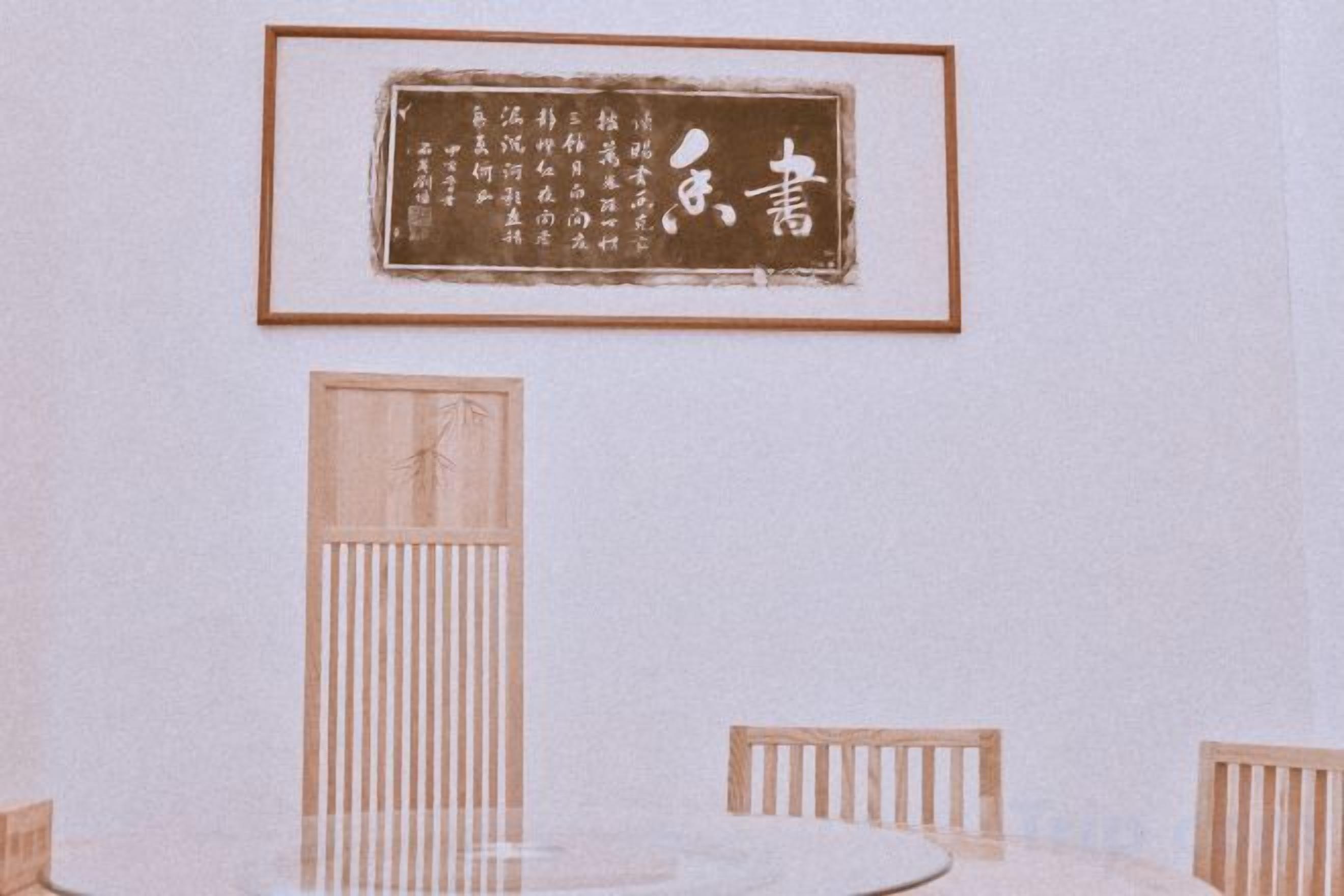 A room with a round table, two chairs, a framed calligraphy piece on the wall, and a vertical wooden panel.