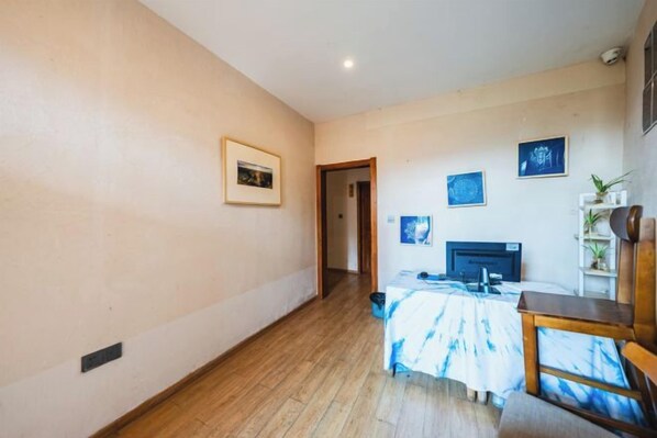 A room with a wooden floor, a bed with a blue and white bedspread, a desk with a computer, and a chair. - Manman Qingfeng Hostel (Xingyi)