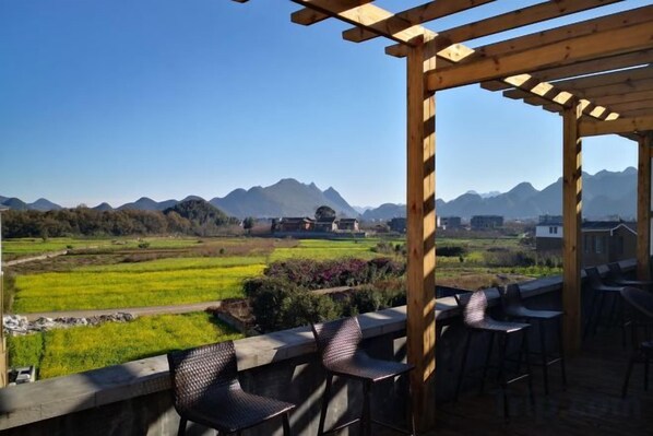 A covered outdoor seating area with a view of a green field and mountains in the distance.