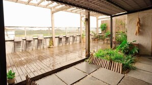 Un espacio al aire libre techado con piso de madera, asientos y plantas en macetas.