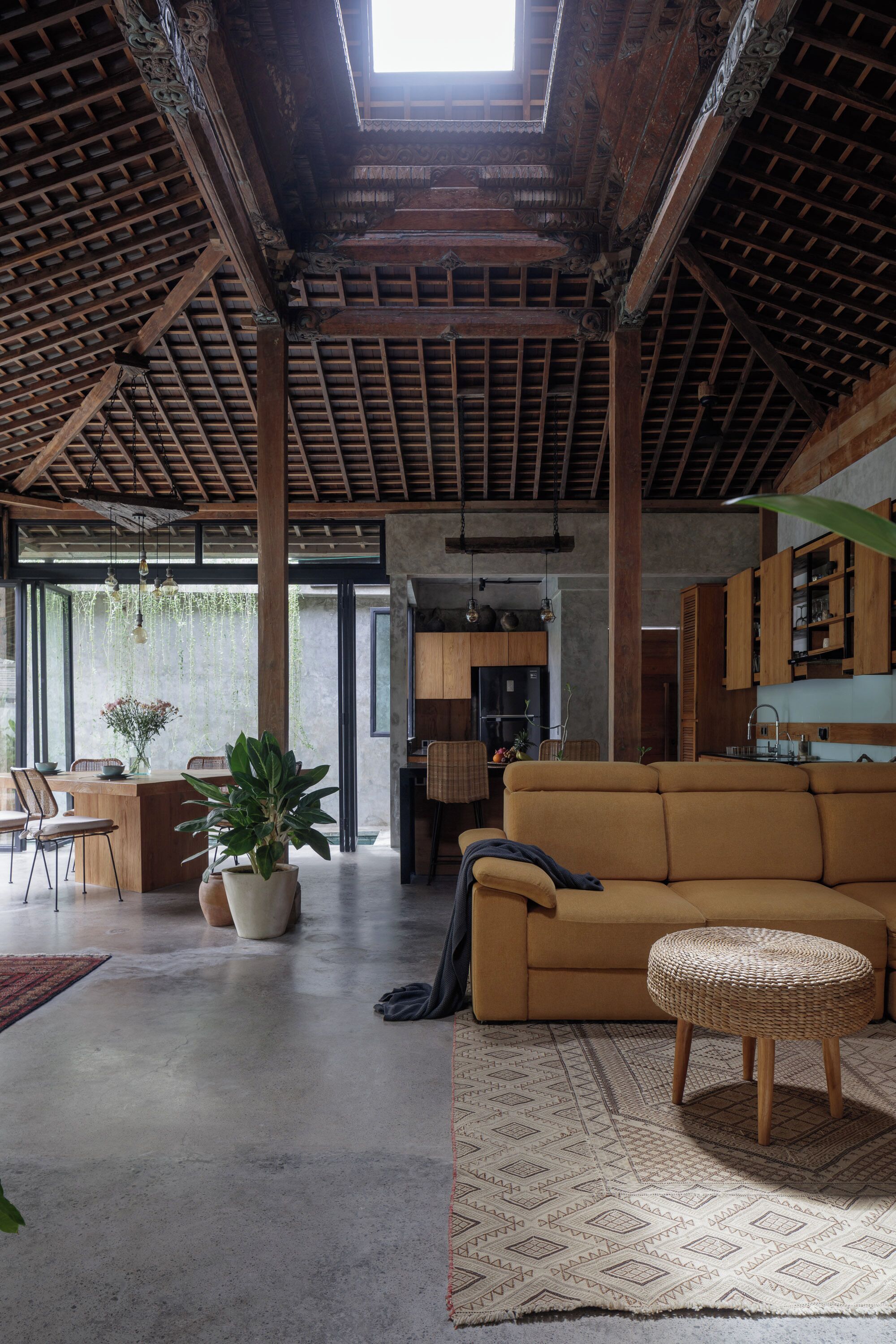 Amplia sala de estar con techo alto, vigas de madera, un sofá, una mesa de comedor y una zona de cocina.