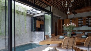 A modern dining area with a wooden table, wicker chairs, and a view of a swimming pool. - Pritidaya Private Pool Villa Canggu by OXO (Canggu)