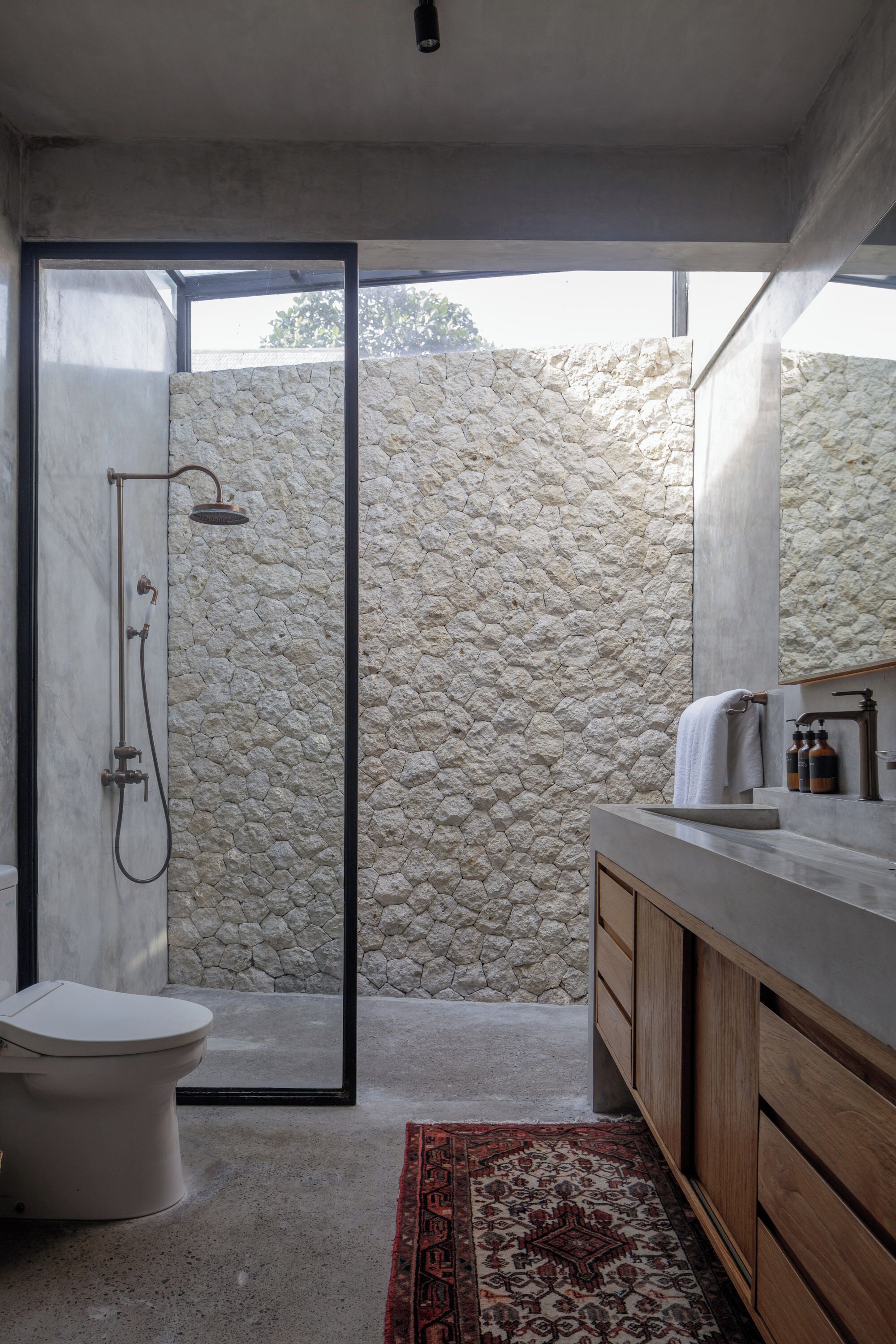 Un baño moderno con pared de piedra, ducha, inodoro y tocador de madera.