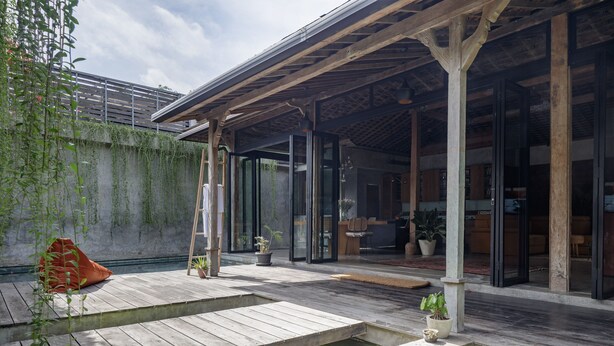 A modern outdoor deck with wooden flooring, glass doors leading to a covered area, and potted plants. - Pritidaya Private Pool Villa Canggu by OXO (Canggu)