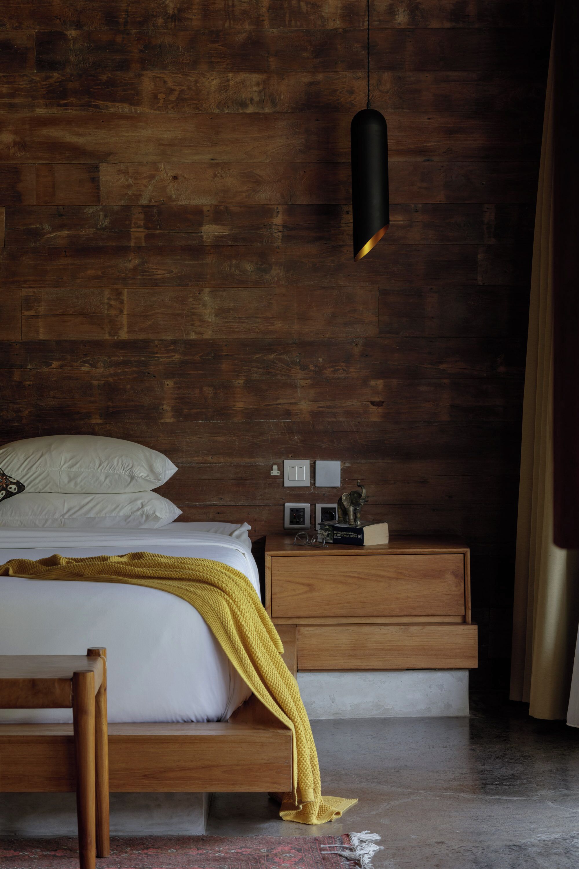 Un dormitorio con una cama de madera, una mesita de noche con una lámpara y un atril con una pequeña estatua.