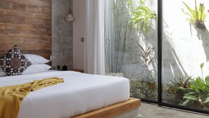 A bedroom with a wooden headboard, white bedding, a yellow throw blanket, and a large window with a view of plants and a bamboo structure. - Pritidaya Private Pool Villa Canggu by OXO (Canggu)